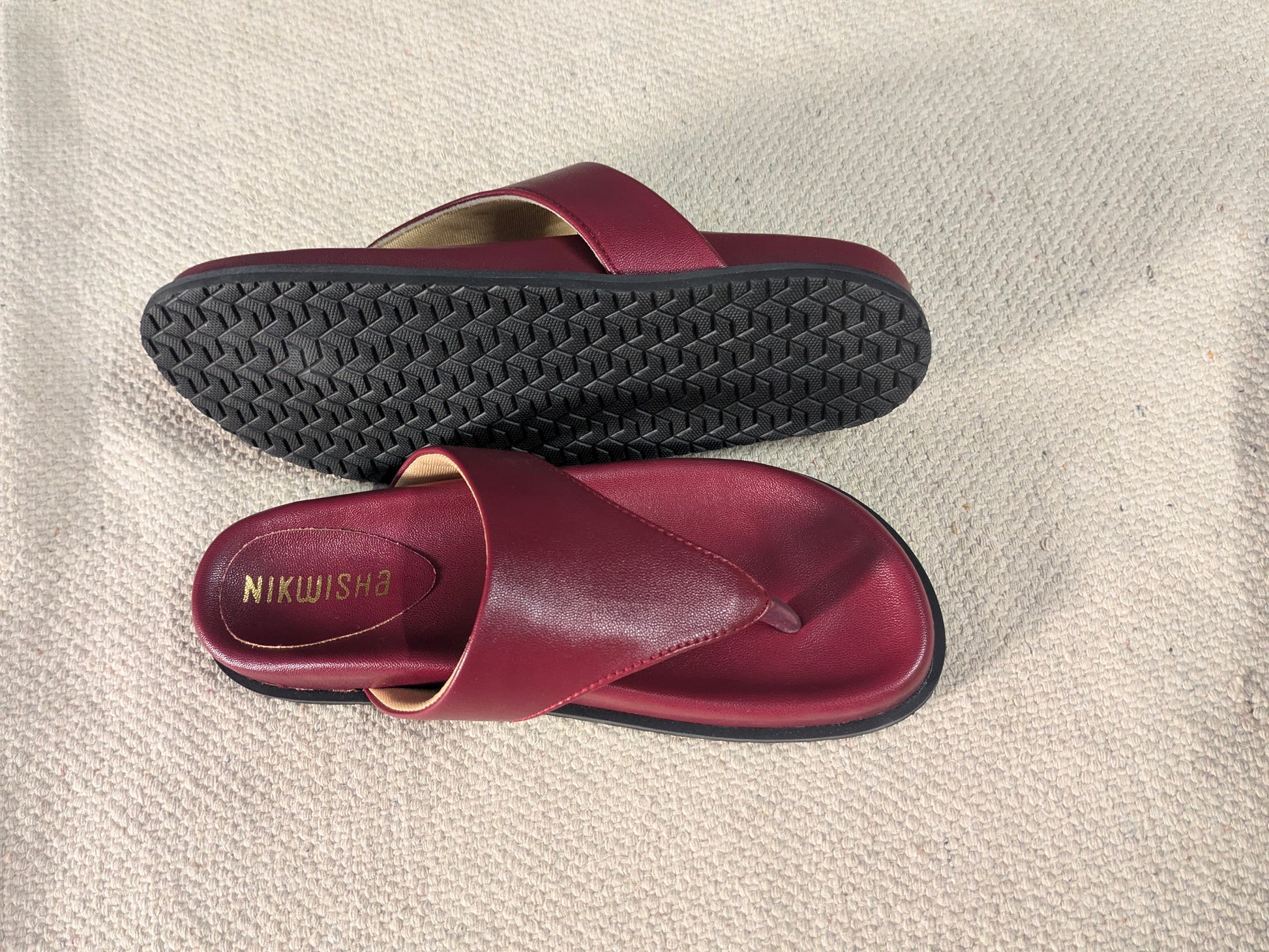Pair of maroon sandals with black soles on a beige textured surface
